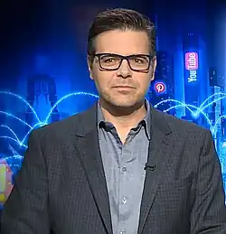 Ein junger Mann von vorne gesehen, sitzend, formell gekleidet und mit Brille.