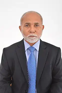 Hussain Rasheed Ahmed, ein dunkelhäutiger älterer Mann mit kurzgeschorenen Haaren im Anzug mit einer blauen Krawatte