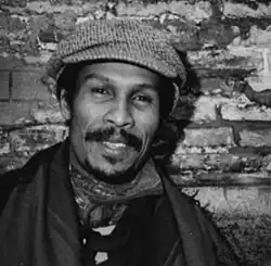 Porträt von Cliff A. Moustache, ca. 1990. Schwarz-Weiß-Porträt eines dunkelhäutigen Mannes mit Schnurrbart und Baskenmütze.