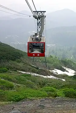 Die rote Gondel einer Seilbahn in begrünter Landschaft ist hier zu sehen.