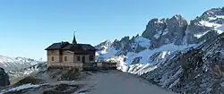 Eine Berghütte auf einem Hügel, im Hintergrund steile Berge