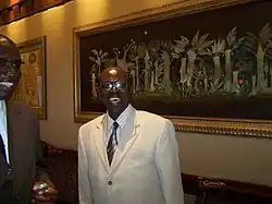 Madior Diouf. 2008 Ein dunkelhäutiger Mann im creme-farbenen Anzug.