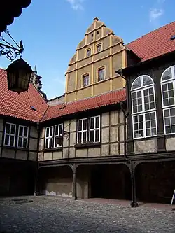 Innenhof eines Fachwerkgebäudes mit roten Ziegeldächern und einem hohen, gestuften Giebel unter blauem Himmel
