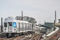 U-Bahn-Zug schlängelt unter Gleisbrücke eine Rampe empor durch Gleisbogen und Weichenstraße bei Tageslicht vor grauem Himmel