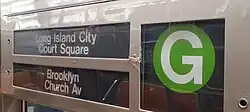 Rollband-Kasten aus grauem lackiertem Blech, drei Felder mit weißer Beschriftung auf schwarzem Grund: „Long Island City / Court Square // Brooklyn / Church Av“ und das hellgrüne runde Signet der Linie G