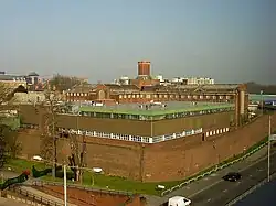 Das Gefängnis in Reading von schräg oben aufgenommen; Gebäudekomplex mit einer umgebenden Backsteinmauer. Im Vordergrund eine Straße mit Autos, im Hintergrund Hochhäuser.