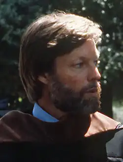 Richard Chamberlain, 1972 hat hellbraunes Haar und trägt ein traditionell anmutendes, langes Gewand in brauner Farbe, das über einem hellblauen Hemd getragen wird. Die Kleidung wirkt schlicht, aber funktional. Luftwaffenminister Verne Orr (nicht im Bild) spricht mit dem Schauspieler Richard Chamberlain, nachdem ihm die Ehrendoktorwürde der Rechtswissenschaften verliehen wurde.