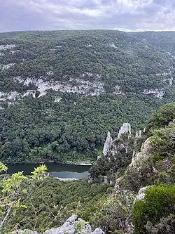 Blick vom Aussichtspunkt hinter der Felsnadel Rocher de la Cathédrale zur Grotte aux Points. Das Höhlenportal ist durch Bäume verdeckt