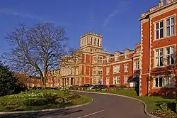 Die Fotografie zeigt das ehemalige Gebäude aus roten Backstein mit mehreren Seitenflügeln und den Vorplatz.