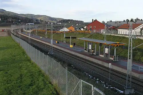 Foto eines Bahnhaltepunktes mit Gleisen im Vordergrund und Wohnhäusern im Hintergrund