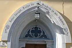 Über dem Eingang des Pfarrhauses steht: „Jesus spricht: Lasset die Kindlein zu mir kommen.“