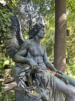 Bronzestatue eines sitzenden, muskulösen Engels mit Lorbeerkranz und Flügeln in einem Park