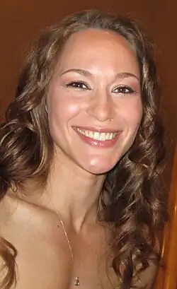 Sharon Taylor bei den Leo Awards 2010 mit braunen, lockigen Haaren, die eine Halskette mit einem kleinen Anhänger trägt. Der Hintergrund ist einfarbig, wahrscheinlich eine schlichte Wand. Es gibt keine weiteren auffälligen Details oder Objekte im Bild.