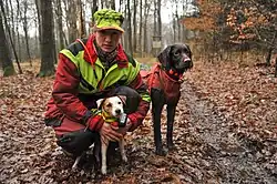 Photo einer Jägerin und zweier Stöberhunde in moderner Bekleidung im Wald während des Herbstes oder Winters.