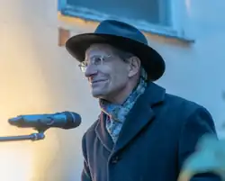 Das Foto zeigt den Dekan Andreas Müller, der nach links blickt und lächelt. Vor ihm ist ein Mikrofon. Links ist eine Lichtquelle.