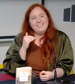 Sophie Lewis, eine weiße Frau mit roten Haaren, lächelnd auf einem Podium.