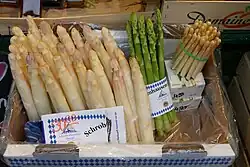 Das Foto zeigt eine Pappkiste von oben, in der verschiedene Spargelsorten zum Verkauf angeboten werden, darunter auch grüner Spargel