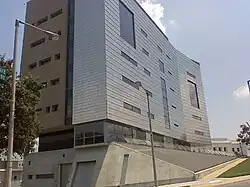 Zweiteiliges Gebäude auf schrägem Betonsockel, auffällige Architektur, vorderer Teil mit heller, hinterer mit dunkler Fassade, unterschiedlich große, asymmetrisch angeordnete Fenster