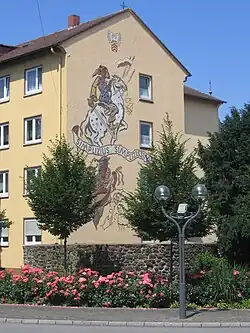 Hauswand mit Sgraffito zur Erinnerung an Grimmelshausens Schelmenroman Simplicius Simplicissimus. Vorn ein Rest der Stadtmauer