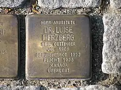 Der Stolperstein trägt die Inschrift: "Hier arbeitete Dr. Luise Herzberg, geb. Oettinger, Jg.1906, Berufsverbot 1933, Flucht 1935, Kanada, überlebt""