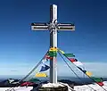 Gipfelkreuz mit Gebetsfahnen und Blick auf Sonnwendstein im Hintergrund