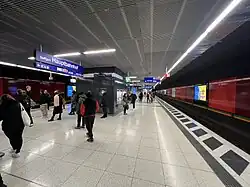 Die unterirdischen S-Bahn-Bahnsteige am Stuttgarter Hauptbahnhof. Eine Menschenmenge befindet sich auf dem Mittelbahnsteig, während sie auf Züge warten.