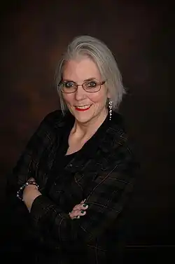 Susan Gerbic Aug 2016. Porträt einer lächelnden älteren Frau mit auffälliger Brille und weißhaarigem Pagenkopf.