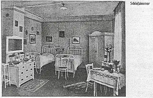 Hell möbliertes Mehrbettzimmer für Schülerinnen mit Metallbetten, Kleiderschrank, Kommode mit Spiegel, kleinem Tisch und Blumenvasen