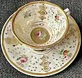 Tasse mit Untertasse. Marken: TPM u. preußischer Adler m. Zepter, Reichsapfel u. Krone (1.1.-13.12.1847) „Eckige Theeform“. Blumenmalerei mit Vergoldungen.