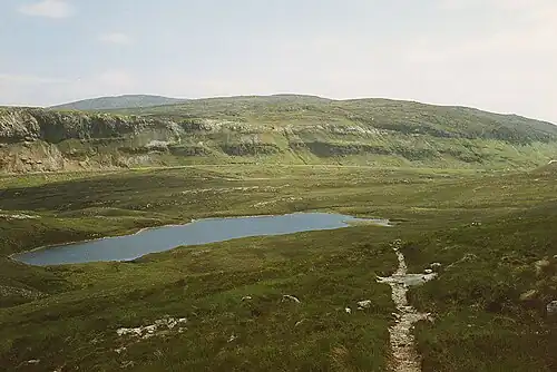Blick vom Aufstiegsweg zurück über den Lochan Fhionnlaidh zur Sole Thrust entlang der A835 road. Kalke der Eilean-Dubh-Formation haben hier das Fucoid Beds Member flach überfahren. Im Hintergrund bereits Gesteine der Moine Supergroup.