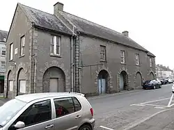 Ein massives, graues, zweistöckiges Gegbäude mit Bogentoren an einer Straße.