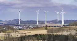 Im Hintergrund 7 Windräder, davor Felder und dazwischen Häuser, teils verdeckt von dem Boden