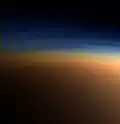 Echtfarbaufnahme der oberen Titan­atmosphäre. In der blauen Dunst­schicht brechen Methan­moleküle auf, darunter liegt der orange­farbene Dunst. Aufnahme aus 9500&nbsp;km Ent­fer­nung, die Auf­lösung beträgt ca. 400&nbsp;m pro Pixel (Cassini, 2005)