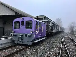 Kleiner violetter Rangiertraktor vor grossen Güterwagen