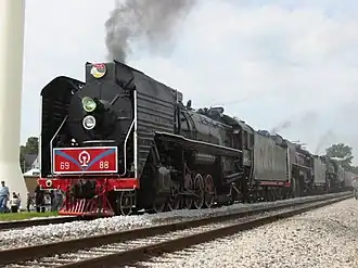 Die zwei QJ-Lokomotiven 6988 und 7081 mit einer dritten Dampflok vor einem Ausflugszug in den USA