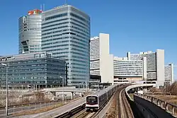 Zug der Type V auf der U1 vor der Skyline der Donau City; im Hintergrund die Station Kaisermühlen&nbsp;– Vienna International Centre