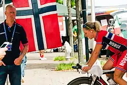 Radrennfahrerin Gotaas Johnsen sitzt auf ihrem Rennrad, ein Betreuer steht in der Nähe