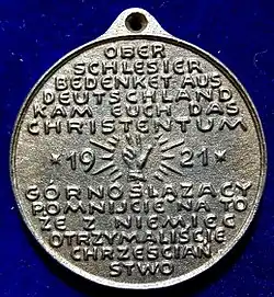 Rückseite der Medaille mit aufgeprägter Schwurhand: „Oberschlesier bedenket, aus Deutschland kam Euch das Christentum“, die das Narrativ der Verbindung von christlicher und deutscher Kultur aufgreift