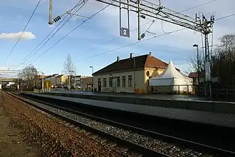 Foto eines Bahnhofsgebäudes mit Gleisen im Vordergrund