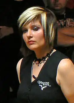 Das Bild zeigt Patricia Murphy in einer Naheinstellung. Ihr Kopf ist leicht nach links gedreht. sie schaut links am Bildausschnitt vorbei und hat einen neutralen Blick aufgesetzt. Sie hat halblange schwarze Haare mit blonden Strähnen und trägt ein schwarzes, ärmelloses Oberteil mit einem weißen Sponsorenlogo sowie eine schwarze Halskette