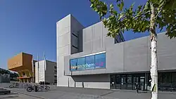 Rechteckiger Gebäude mit breiter Fensterfront im Erdgeschoss und ersten Stock.